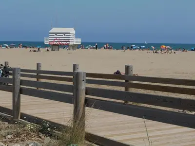 a wooden fence on a beach with a building in the background at Studio spacieux à Gruissan - Parking - Vue port - Proche plage - FR-1-796-29 in Gruissan