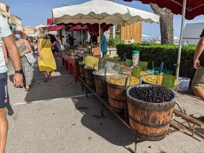 a group of people standing around a market with grapes in barrels at T3 spacieux climatisé - 5 pers - près plage, centre & animations - Parking privé - FR-1-797-22 in Port-la-Nouvelle