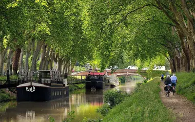 a river with a bridge and people riding bikes on a canal at Evasion dépaysante Canal du Midi La vie en couleur in Castelnaudary