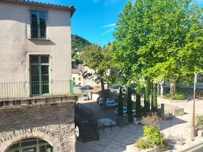 a building with a balcony next to a tree at Le petit paradis in Saint-Pons-de-Thomières