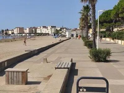a beach with benches and people walking on the beach at Gruissan - T2 Mezzanine Climatisé - 6 Pers - Parking Proche Plage - FR-1-796-87 in Gruissan