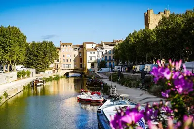 a river with boats and buildings and purple flowers at L'Appart Central - Chic et Confort in Narbonne