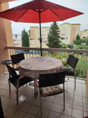 a table and chairs with a red umbrella on a balcony at 2 appartements mitoyens avec climatisation, piscine et parking - Plages et Port à 100m in Gruissan