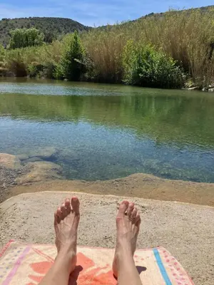 a persons feet on a blanket next to a body of water at L'Ecurie in Paziols