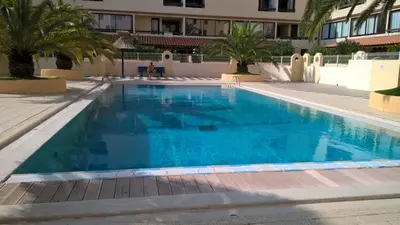 a large blue swimming pool with palm trees and a building at Les Drom's studio in Gruissan