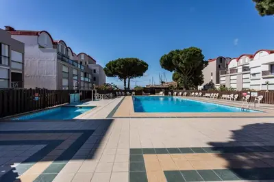 a swimming pool with chairs and trees and buildings at Studio Gruissan La Presqu'île 2 in Gruissan