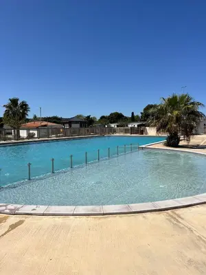 a large swimming pool with blue water and palm trees at Les mobil homes de NOLY TV CLIM 6places in Port-la-Nouvelle